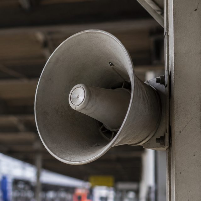 A weathered metal horn speaker — the kind that looks exactly as tinny and hard to make out as it sounds.